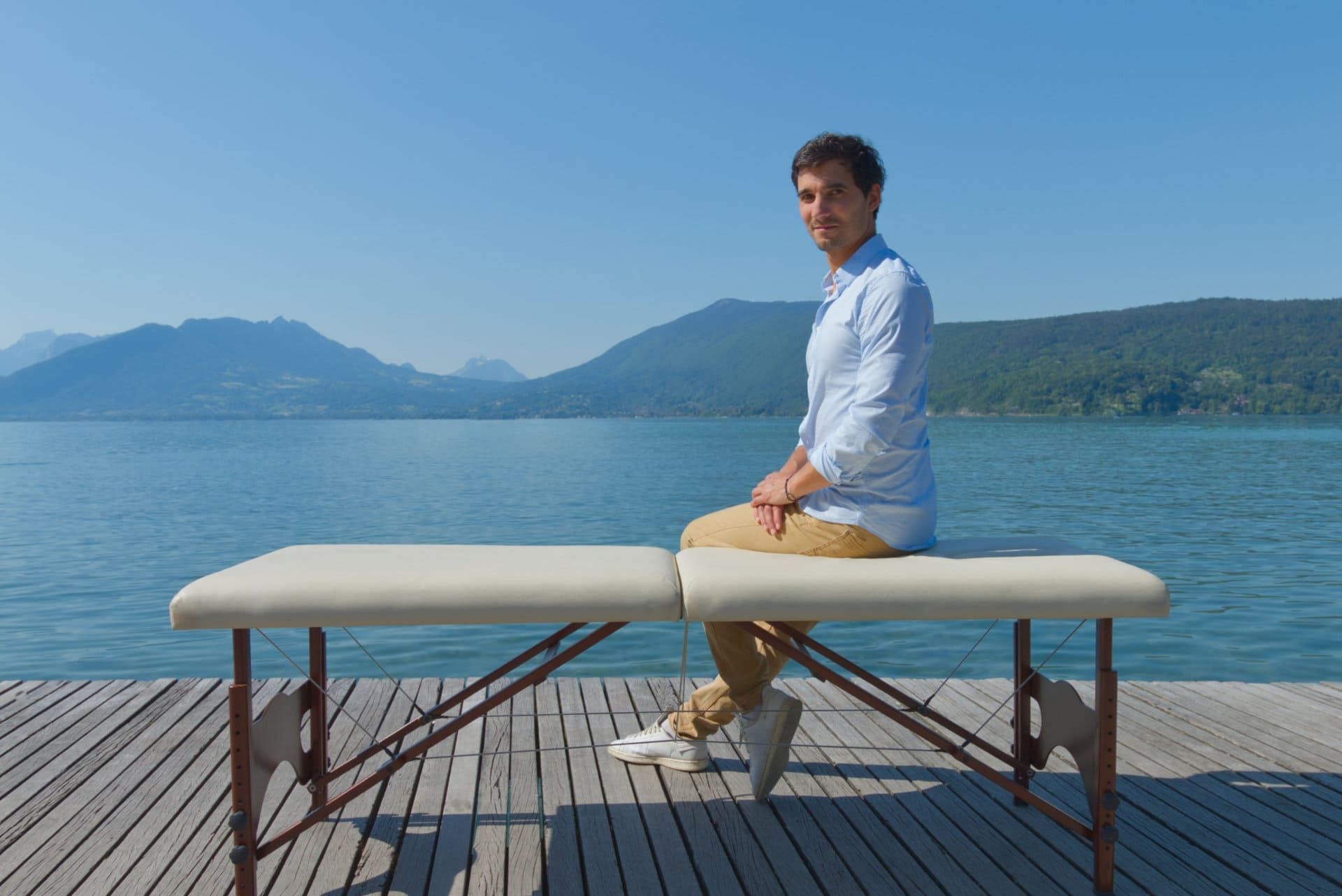 Jordi Baux, ostéopathe, assis sur une table de soin au bord du lac d’Annecy